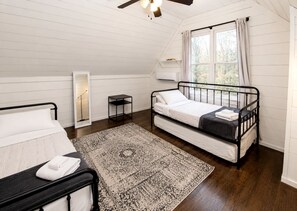 Ein Schlafzimmer mit einem Bett, einem Nachttisch, einer Stehlampe, einem Fenster mit Vorhängen und einem Deckenventilator.