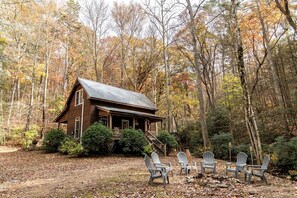 A cabin with a porch, surrounded by trees and a dirt path.