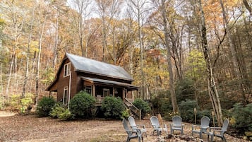 A cabin with a porch, surrounded by trees and a dirt path.