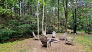 Entorno boscoso con una fogata y sillones Adirondack.