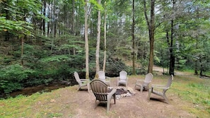 A forest setting with a fire pit and Adirondack chairs. - Secluded Cabin on Suches Creek and in the National Forest for a Relaxing Georgia Getaway (Suches)