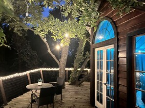 An outdoor deck with a table and chairs, surrounded by string lights and a tree.