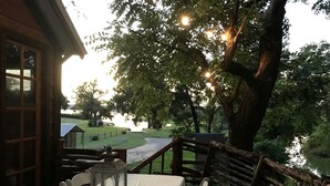 An outdoor dining area with a table set for two, a lantern, and a view of a river and greenery. - Creekside Texas Tree House Rental on Lake Conroe (Willis)
