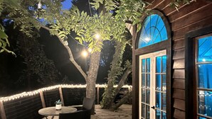 An outdoor deck with a table and chairs, surrounded by string lights and a tree. - Creekside Texas Tree House Rental on Lake Conroe (Willis)
