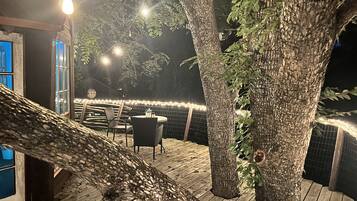 An outdoor patio with a wooden deck, a table with chairs, and string lights.