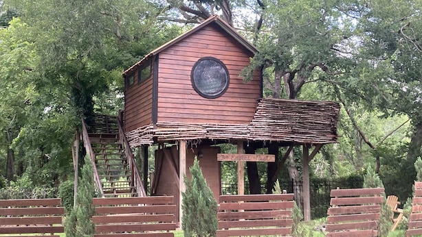 A wooden treehouse with a circular window and a sign that reads 'The Eagles Nest.' - Creekside Texas Tree House Rental on Lake Conroe (Willis)