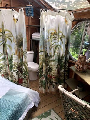 A wooden cabin interior with a bed, a toilet, and a window with a view of greenery.