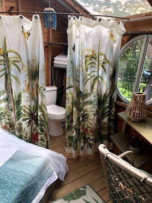 Interior de una cabaña de madera con una cama, un inodoro y una ventana con vistas a la vegetación.
