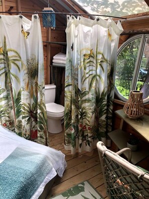 A wooden cabin interior with a bed, a toilet, and a window with a view of greenery. - Gorgeous Tree House Rental with Lake Views for Glamping in Texas (Willis)