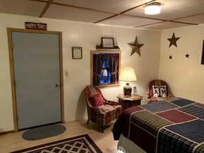 A room with a door labeled 'Happy Trails,' a patterned armchair, a bed with a quilt, a lamp, and a star decoration on the wall. - Clear River Cabin on the Medina River in Bandera, Texas (Bandera)