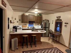 Cocina compacta con una isla central, armarios de madera, un refrigerador y un comedor con una silla y mesa.
