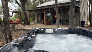 Un bain à remous doté d’une terrasse en bois rustique, d’un espace salon couvert et offrant une vue sur un chalet.