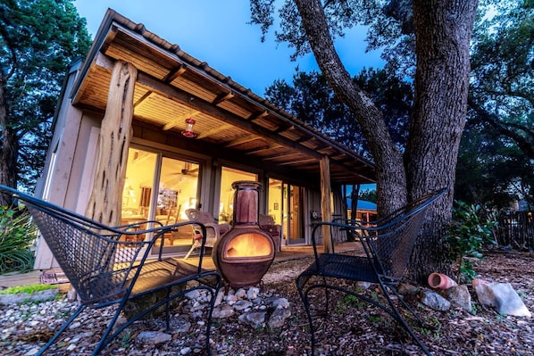 A rustic cabin with a large window, a hanging light fixture, and a large vase on the porch.