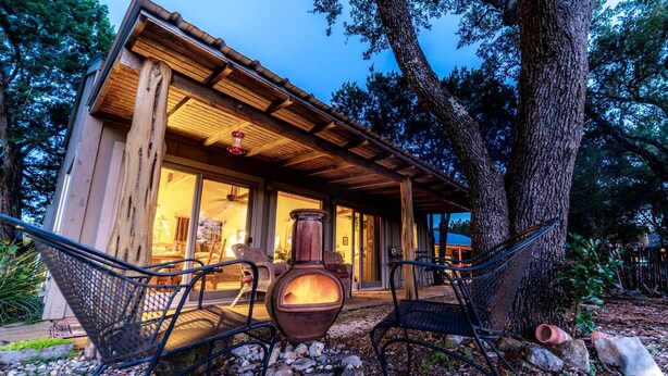 A rustic cabin with a large window, a hanging light fixture, and a large vase on the porch.