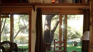 A wooden interior with a view of a lake and trees, a chair, and a table with a plate and a book.