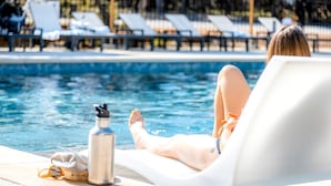 Une personne se détend au bord d’une piscine, avec des chaises longues et une bouteille d’eau en premier plan.