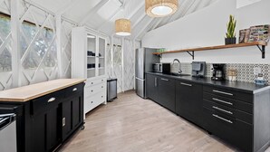 Una cocina moderna con encimera de madera, armarios negros, microondas integrado y una lámpara colgante.