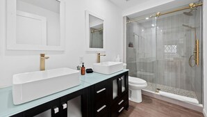Une salle de bain moderne avec deux lavabos, des toilettes et une douche à parois de verre.