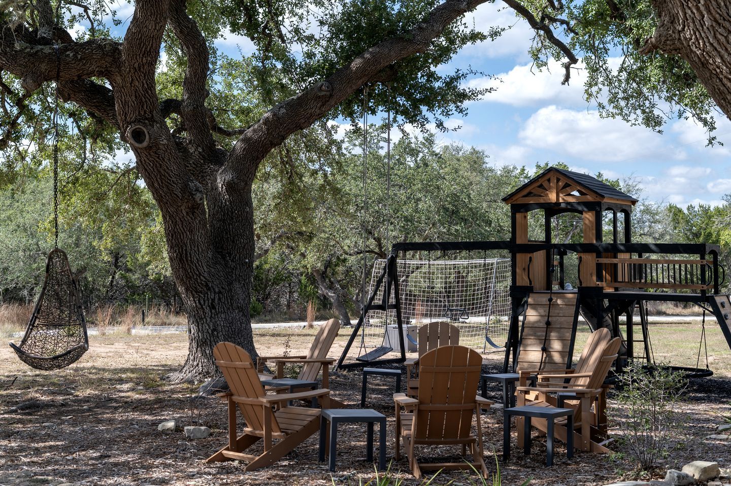 A treehouse with a swing set, surrounded by wooden chairs and tables.