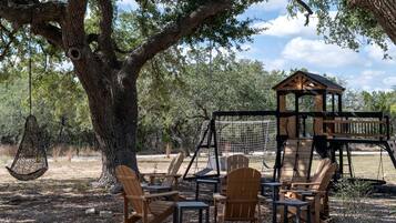 A treehouse with a swing set, surrounded by wooden chairs and tables.