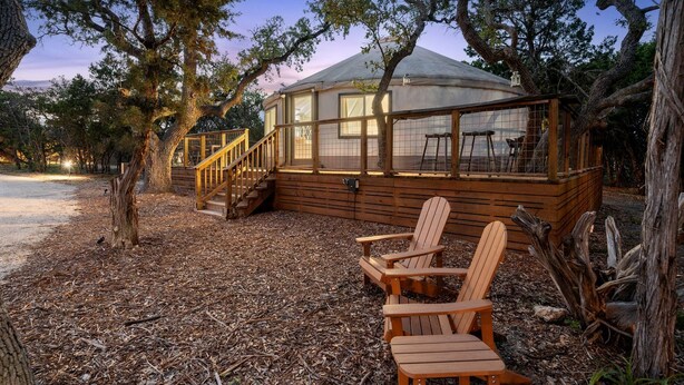 Une yourte dotée d’une terrasse en bois et de chaises, entourée d’arbres.