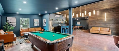 Una mesa de billar en una habitación con pared azul, un panel de madera decorativo y una zona de bar.