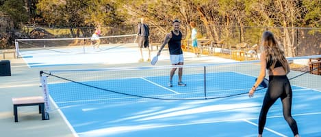 Un campo da tennis all'aperto con rete, panchine e recinzione.