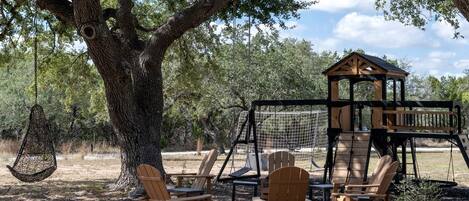 Una casa en árbol con un columpio, rodeada de sillas y mesas de madera.