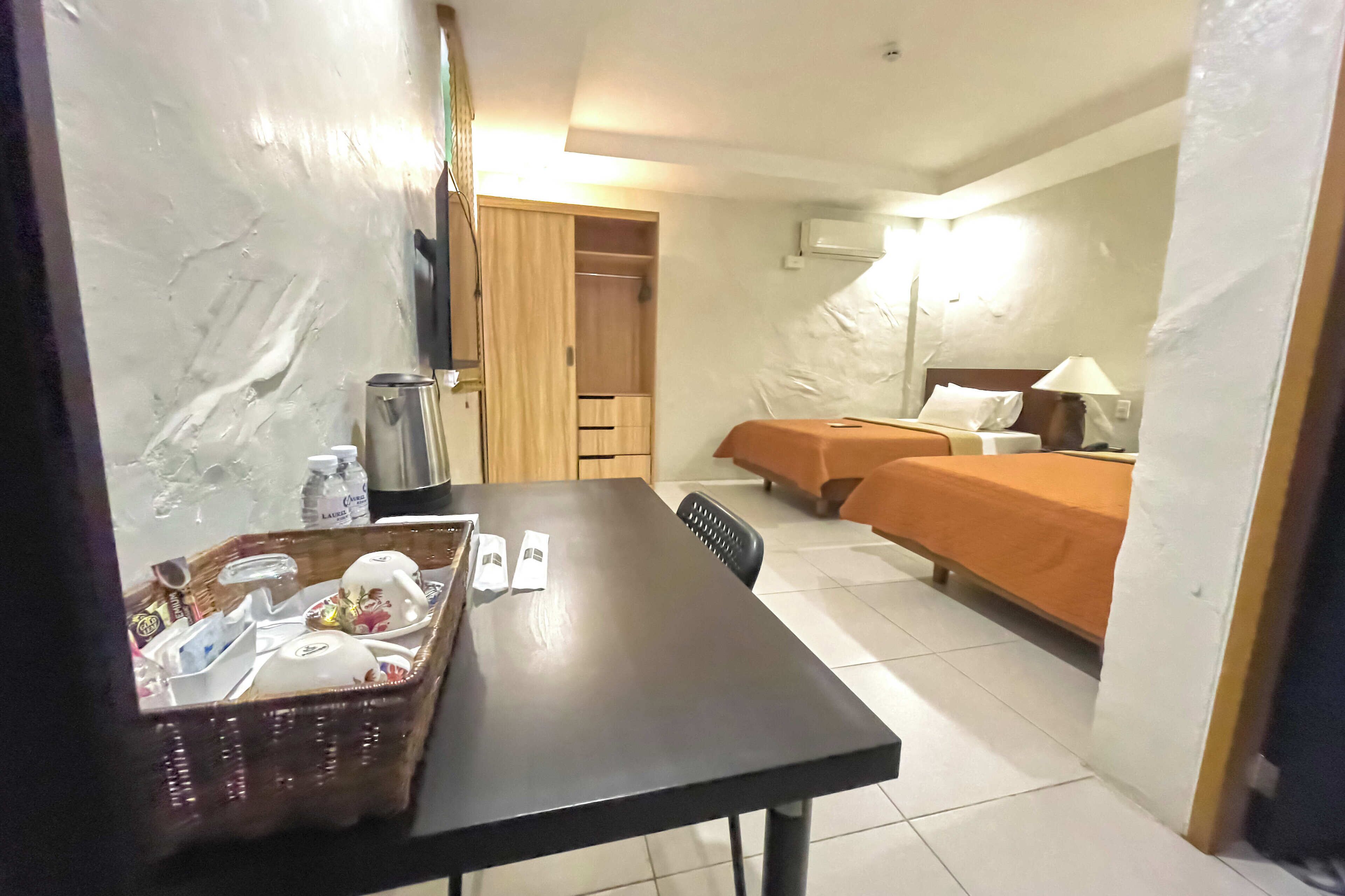 A hotel room with a dining table, two beds, a wardrobe, and a small kitchenette.