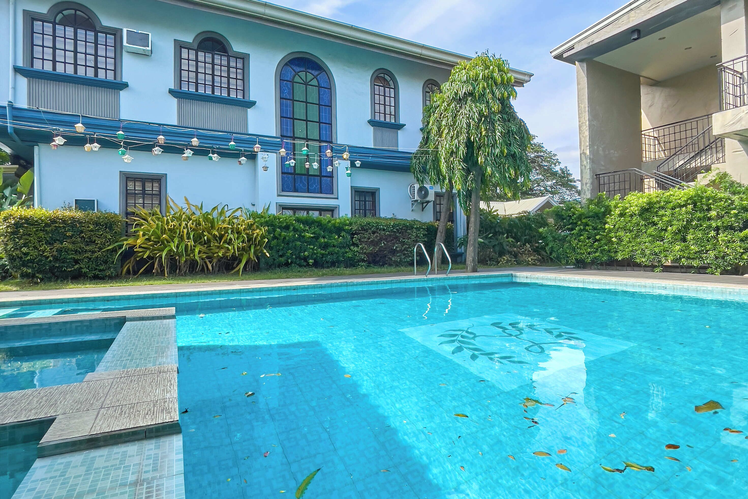 Piscina com degraus para acesso, cercada por vegetação e um edifício com janelas amplas e uma varanda.
