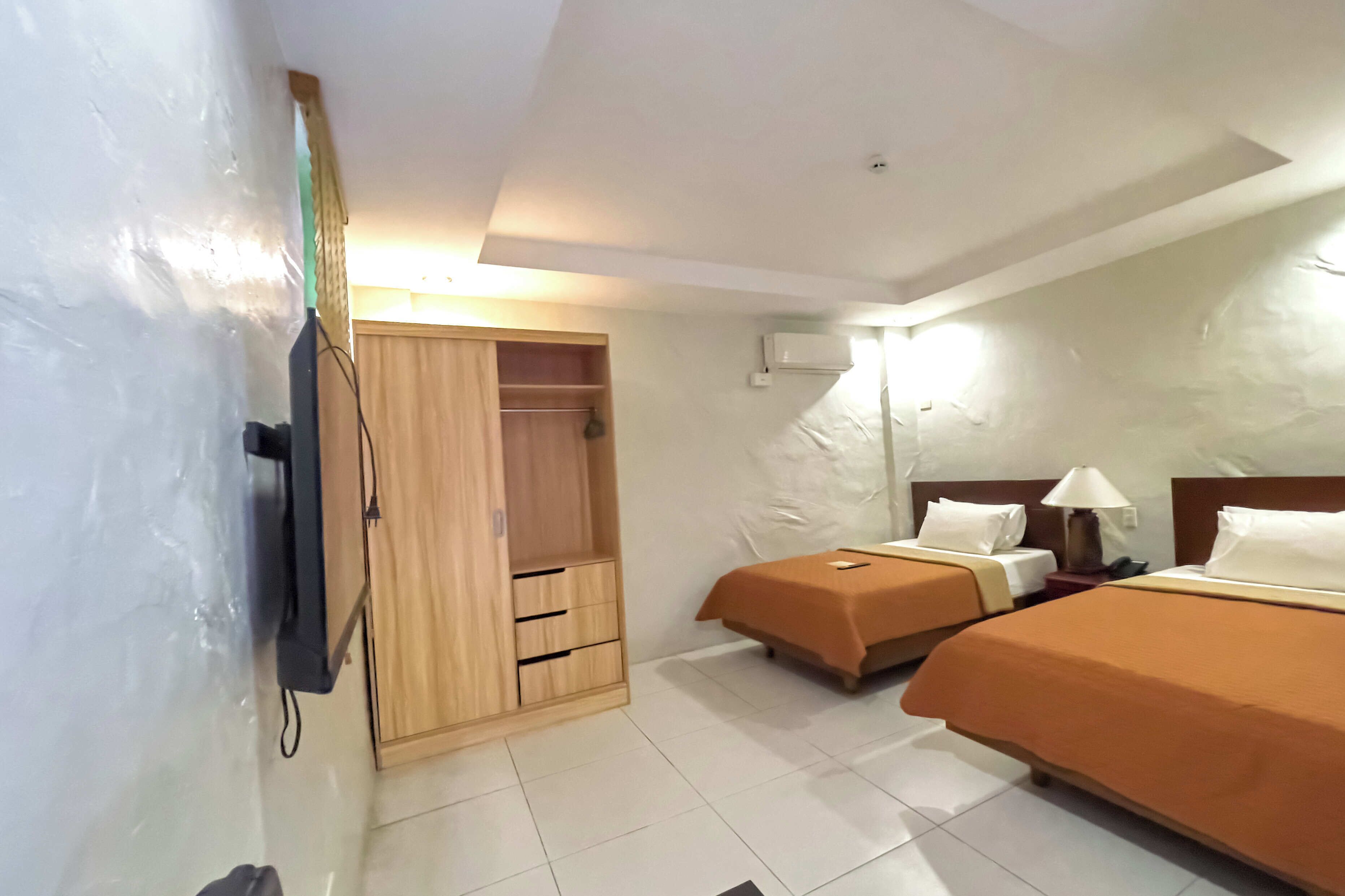 Habitación de hotel con dos camas, un armario de madera, un televisor y un aire acondicionado instalado en la pared.