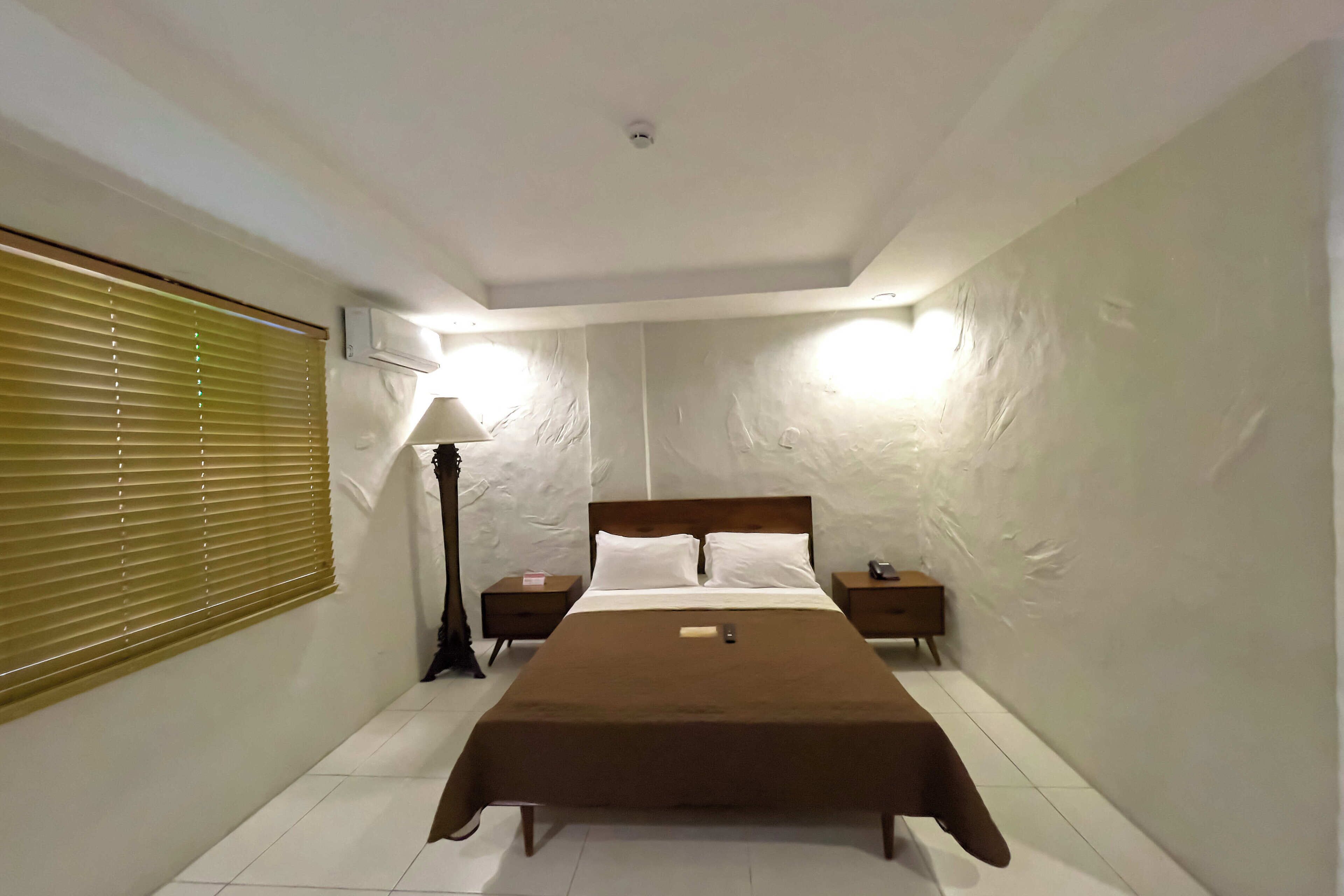 Une chambre avec un lit simple, deux tables de chevet, une lampe et un luminaire au plafond.
