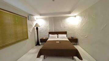 A bedroom with a large bed, two bedside tables, a lamp, and a window with blinds.