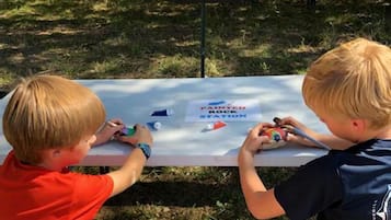 Two children painting on a table outdoors with a sign in the background.