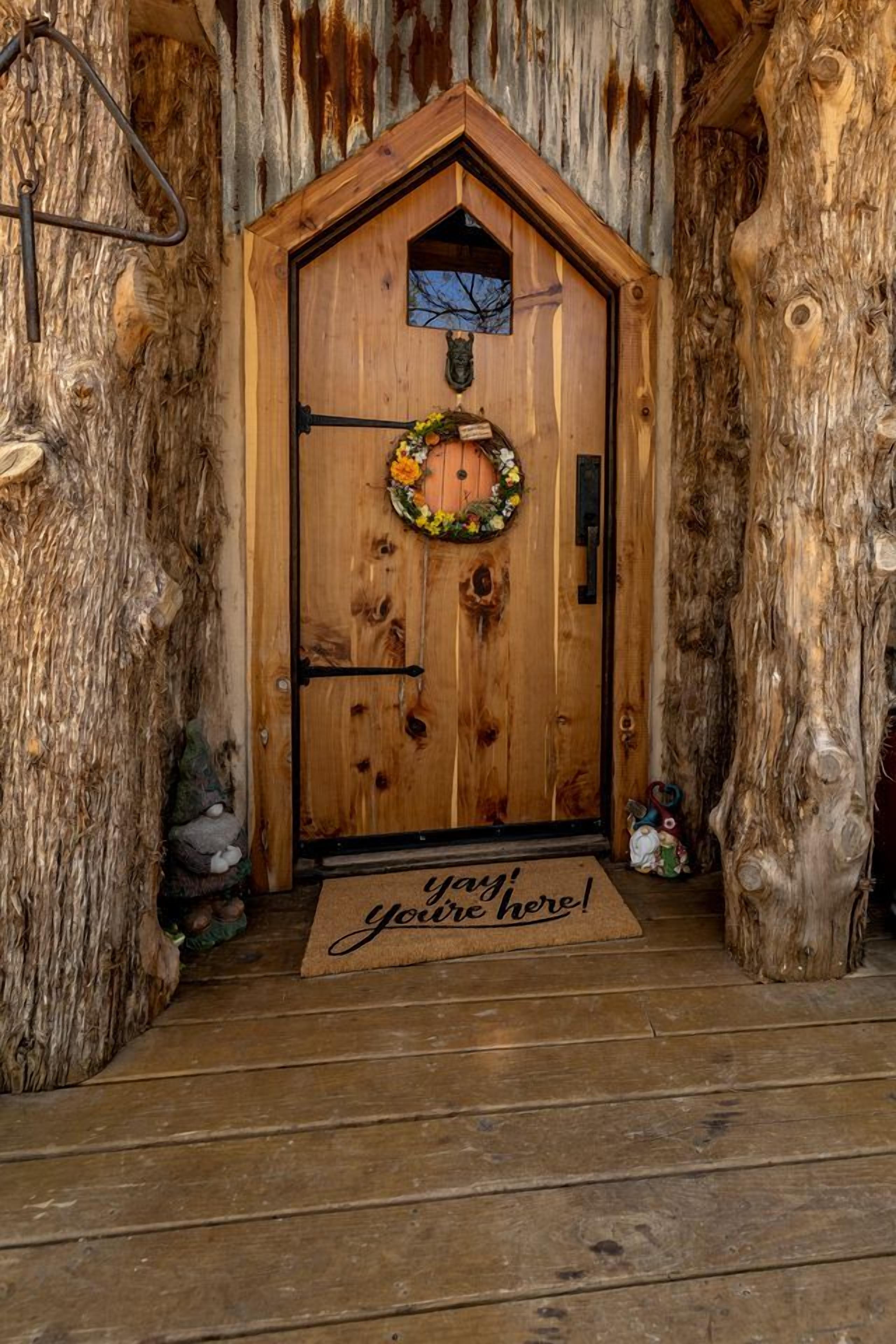 A wooden door with a wreath, a doormat with 'you're here!' text, and a rustic interior.