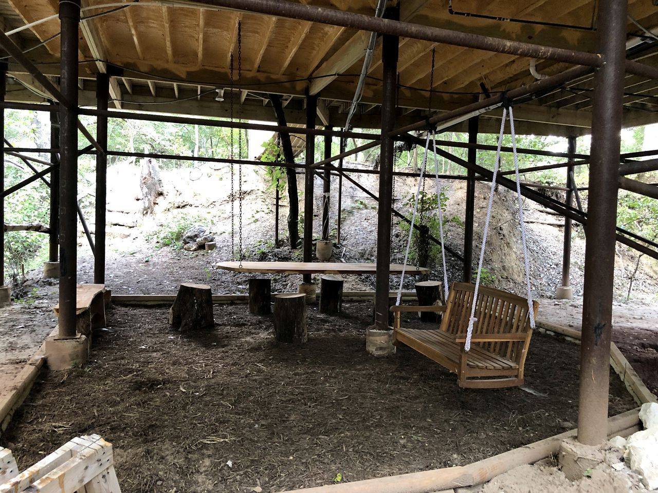 Un espace extérieur abrité comprenant un banc en bois, une balançoire et une table.