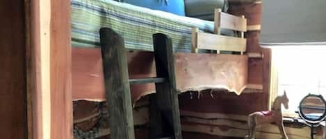 Ein Holzhütten-Innenraum mit Etagenbett, einer Leiter, einem kleinen Tisch und einem Spiegel sowie einem Ventilator.