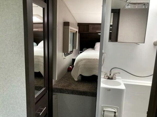 A compact bedroom with a single bed, a small window, a mirror, and a sink. - Tiny Caravan Great for Couples with Landscape Views in Idaho (Saint Maries)