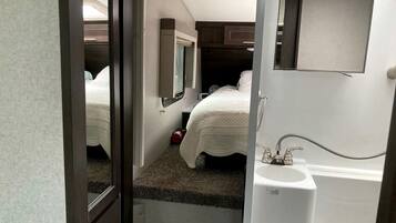 Un dormitorio pequeño con una cama individual, una ventana, un espejo y un lavabo.