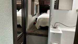 Un dormitorio pequeño con una cama individual, una ventana, un espejo y un lavabo.