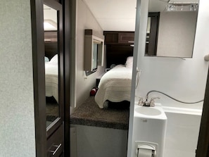 A compact bedroom with a single bed, a small window, a mirror, and a sink. - Tiny Caravan Great for Couples with Landscape Views in Idaho (Saint Maries)