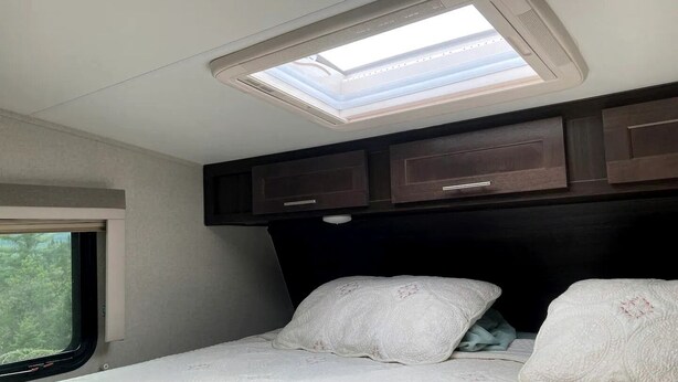 A bedroom with a skylight, a window, and a bed with pillows. - Tiny Caravan Great for Couples with Landscape Views in Idaho (Saint Maries)