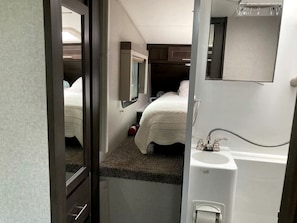 Une chambre à coucher de taille modeste, avec un lit simple, une petite fenêtre, un miroir et un lavabo.