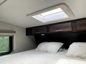 A bedroom with a skylight, a window, and a bed with pillows.