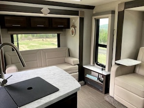 A kitchen area with a sink, a countertop, and a window. There is a seating area with a sofa and a chair. - Tiny Caravan Great for Couples with Landscape Views in Idaho (Saint Maries)