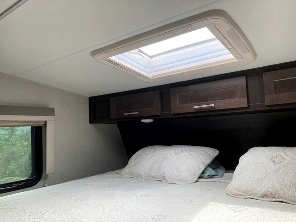 Une chambre avec un puits de lumière, une fenêtre et un lit avec des oreillers.
