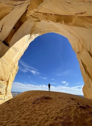 A person standing in a natural rock arch formation with a clear blue sky above. - Pet Friendly Dry Tent Near for Glamping near Zion National Park (Hildale)