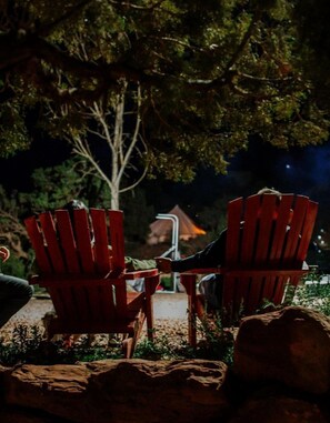 Zwei rote Adirondack-Stühle im Freien bei Nacht, mit einem Baum und einem Gebäude im Hintergrund.