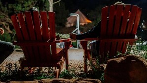Deux chaises Adirondack rouges sont placées à l’extérieur, de nuit, avec un arbre et un bâtiment en arrière-plan.