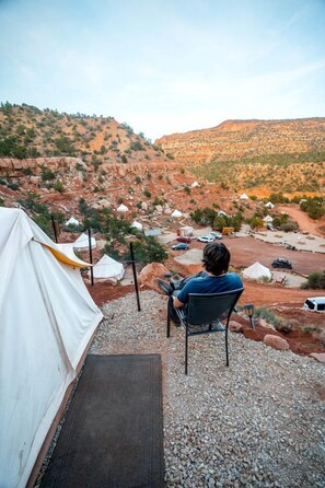 Una persona sentada a una mesa con vista a un camping con tiendas de campaña y vehículos.